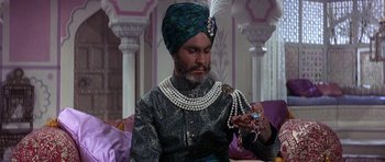 Movie still from “The Pink Panther” (1963), directed by Blake Edwards – A man wearing a turban and a turban is looking at a necklace; Medium shot, High angle