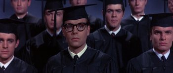 Movie still from “The Pink Panther” (1963), directed by Blake Edwards – A man in a cap and gown stands in front of a group of men; Close Up shot, Over the shoulder angle