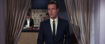 Movie still from “The Pink Panther” (1963), directed by Blake Edwards – A man in a suit and tie standing in front of a bar; Close Up shot, Low angle