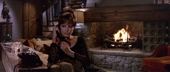 Movie still from “The Pink Panther” (1963), directed by Blake Edwards – A woman sitting in front of a fireplace holding a cell phone; Medium shot, High angle