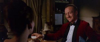 Movie still from “The Pink Panther” (1963), directed by Blake Edwards – A man sitting at a table with a drink in front of him; Medium shot, Over the shoulder angle