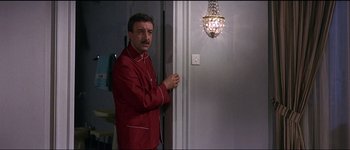 Movie still from “The Pink Panther” (1963), directed by Blake Edwards – A man standing in front of a door in front of a light fixture; Medium shot, Over the shoulder angle