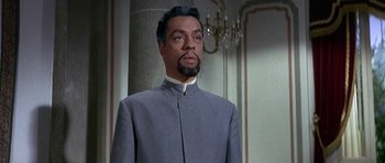 Movie still from “The Pink Panther” (1963), directed by Blake Edwards – A man with a beard wearing a gray suit and white shirt; Medium shot, Low angle