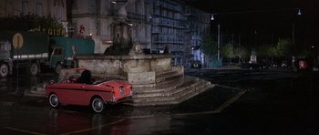 Movie still from “The Pink Panther” (1963), directed by Blake Edwards – An old red car parked in front of a fountain at night; Wide shot, High angle