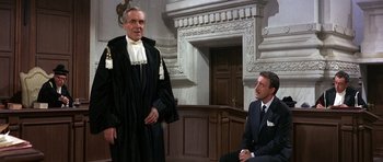 Movie still from “The Pink Panther” (1963), directed by Blake Edwards – Two men in suits sitting in front of a judge; Medium shot, Over the shoulder angle