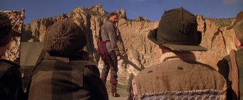 Movie still from “The Postman” (1997), directed by Kevin Costner – A man holding an axe in a mountainous area; Wide shot, Low angle