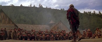 Movie still from “The Postman” (1997), directed by Kevin Costner – A large group of people sitting in front of a building; Wide shot, Over the shoulder angle