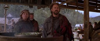 Movie still from “The Postman” (1997), directed by Kevin Costner – Two men standing next to each other near a wooden barrel; Medium shot, Low angle
