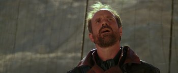 Movie still from “The Postman” (1997), directed by Kevin Costner – A man with a beard is looking up at the sky; Close Up shot, Low angle