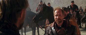 Movie still from “The Postman” (1997), directed by Kevin Costner – A man sitting next to a brown horse on top of a dirt field; Close Up shot, Over the shoulder angle