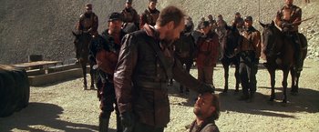 Movie still from “The Postman” (1997), directed by Kevin Costner – A group of men standing next to each other on top of a hill; Medium shot, Over the shoulder angle