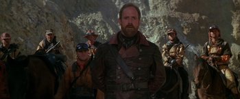 Movie still from “The Postman” (1997), directed by Kevin Costner – A group of men standing next to each other in a cave; Medium shot, Low angle