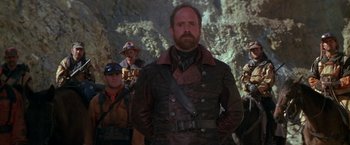 Movie still from “The Postman” (1997), directed by Kevin Costner – A group of men standing next to each other in a cave; Medium shot, Low angle