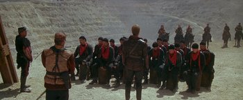 Movie still from “The Postman” (1997), directed by Kevin Costner – A group of men sitting in a formation on top of a mountain; Wide shot, High angle