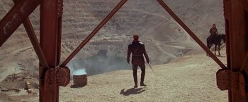 Movie still from “The Postman” (1997), directed by Kevin Costner – A man standing on top of a mountain holding a sword; Extreme Wide shot, High angle