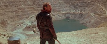 Movie still from “The Postman” (1997), directed by Kevin Costner – A man standing in front of an open pit; Wide shot, Low angle