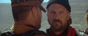 Movie still from “The Postman” (1997), directed by Kevin Costner – A man with a beard is looking at another man with a beard; Close Up shot, Over the shoulder angle