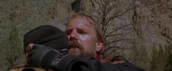 Movie still from “The Postman” (1997), directed by Kevin Costner – A man with a beard is holding his head down; Close Up shot, Over the shoulder angle