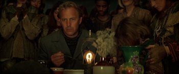 Movie still from “The Postman” (1997), directed by Kevin Costner – A man sitting at a table with a candle in the middle of the table; Medium shot, Low angle