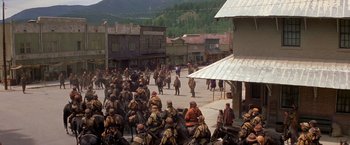 Movie still from “The Postman” (1997), directed by Kevin Costner – A group of men riding horses down a street; Extreme Wide shot, High angle