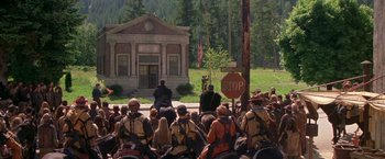 Movie still from “The Postman” (1997), directed by Kevin Costner – A group of people sitting in front of a building on a street; Extreme Wide shot, High angle