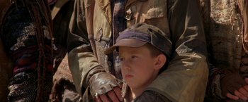 Movie still from “The Postman” (1997), directed by Kevin Costner – A young boy in a hat holding a cane; Close Up shot, Over the shoulder angle