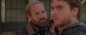 Movie still from “The Postman” (1997), directed by Kevin Costner – A man with a goatee and a beard is looking at another man with a goatee; Close Up shot, Over the shoulder angle