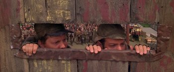 Movie still from “The Postman” (1997), directed by Kevin Costner – A group of people standing next to each other on top of a field; Medium shot, Over the shoulder angle