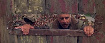 Movie still from “The Postman” (1997), directed by Kevin Costner – A group of people in the background of a picture of a man; Medium shot, Over the shoulder angle
