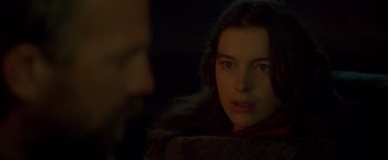 Movie still from “The Postman” (1997), directed by Kevin Costner – A young woman looking at the camera in a dimly - lit room; Close Up shot, Over the shoulder angle