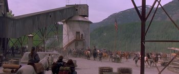 Movie still from “The Postman” (1997), directed by Kevin Costner – A group of people riding horses near a building; Extreme Wide shot, High angle