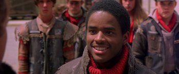 Movie still from “The Postman” (1997), directed by Kevin Costner – A young man smiles for the camera in front of a group of people; Close Up shot, Low angle
