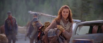 Movie still from “The Postman” (1997), directed by Kevin Costner – A young woman is walking with a backpack and gloves; Medium shot, Over the shoulder angle