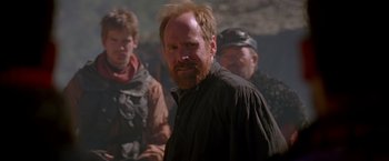 Movie still from “The Postman” (1997), directed by Kevin Costner – A man standing next to a group of people; Close Up shot, Over the shoulder angle