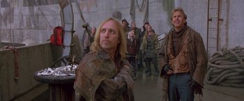 Movie still from “The Postman” (1997), directed by Kevin Costner – A group of people standing in a room; Medium shot, Over the shoulder angle