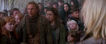 Movie still from “The Postman” (1997), directed by Kevin Costner – A group of people standing around each other in a room; Medium shot, Low angle