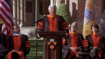 Movie still from “The Princess Diaries 2: Royal Engagement” (2004), directed by Garry Marshall – An older man in a graduation gown speaking at a podium; Wide shot, High angle
