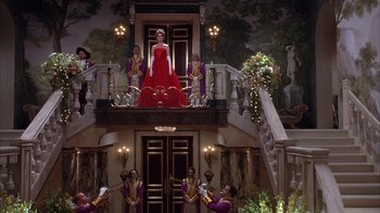 Movie still from “The Princess Diaries 2: Royal Engagement” (2004), directed by Garry Marshall – A woman in a red dress standing on a balcony; Wide shot, Low angle