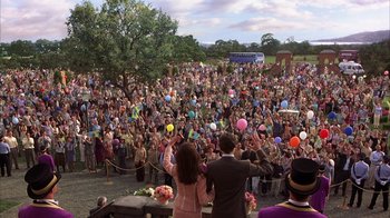 Movie still from “The Princess Diaries 2: Royal Engagement” (2004), directed by Garry Marshall – A crowd of people standing in front of a stage with balloons; Extreme Wide shot, High angle