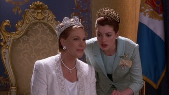 Movie still from “The Princess Diaries 2: Royal Engagement” (2004), directed by Garry Marshall – Two women in a room wearing tiaras and wearing necklaces; Close Up shot, Over the shoulder angle