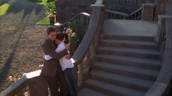 Movie still from “The Princess Diaries 2: Royal Engagement” (2004), directed by Garry Marshall – A man and a woman hugging near a staircase; Wide shot, High angle