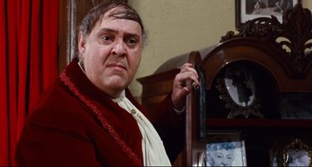 Movie still from “The Producers” (1967), directed by Mel Brooks – An older man in a red jacket is holding a clock; Close Up shot, Over the shoulder angle