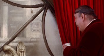 Movie still from “The Producers” (1967), directed by Mel Brooks – A man holding a coffee cup in front of a red curtain; Medium shot, Over the shoulder angle