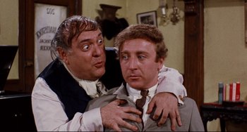 Movie still from “The Producers” (1967), directed by Mel Brooks – A man holding another man in his arms in a room; Medium shot, Over the shoulder angle