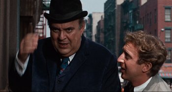 Movie still from “The Producers” (1967), directed by Mel Brooks – A man in a suit and a man in a top hat talking; Close Up shot, Over the shoulder angle