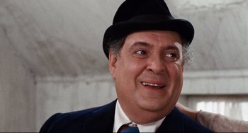 Movie still from “The Producers” (1967), directed by Mel Brooks – A man in a suit and hat smiling for the camera; Close Up shot, Over the shoulder angle