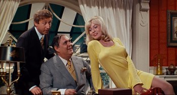 Movie still from “The Producers” (1967), directed by Mel Brooks – A woman in a yellow dress standing next to two men; Medium shot, Over the shoulder angle