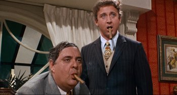 Movie still from “The Producers” (1967), directed by Mel Brooks – Two men in suits and ties are smoking a cigar; Medium shot, Low angle