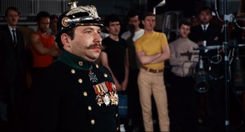 Movie still from “The Producers” (1967), directed by Mel Brooks – A group of men standing around a man in a military uniform; Medium shot, Over the shoulder angle