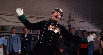Movie still from “The Producers” (1967), directed by Mel Brooks – A man in a military uniform is singing in front of a crowd; Medium shot, Low angle